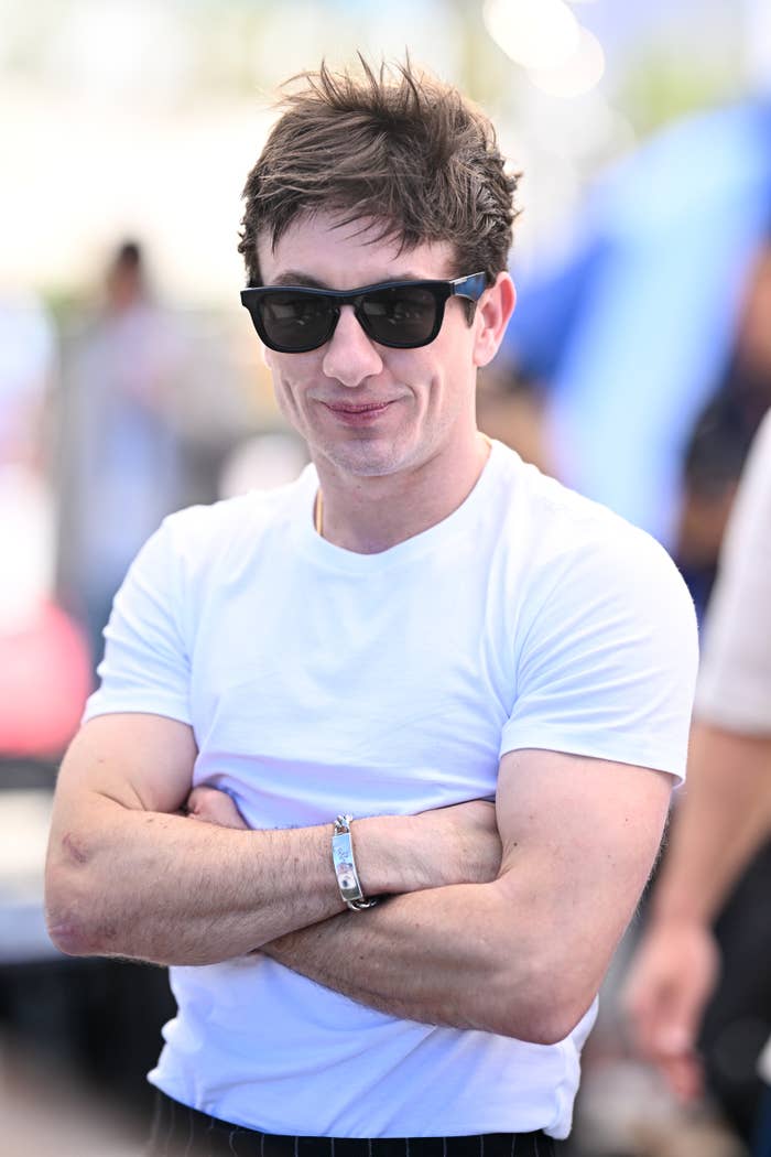Barry Keoghan wearing sunglasses and a white t-shirt, smiling with arms crossed at an outdoor event