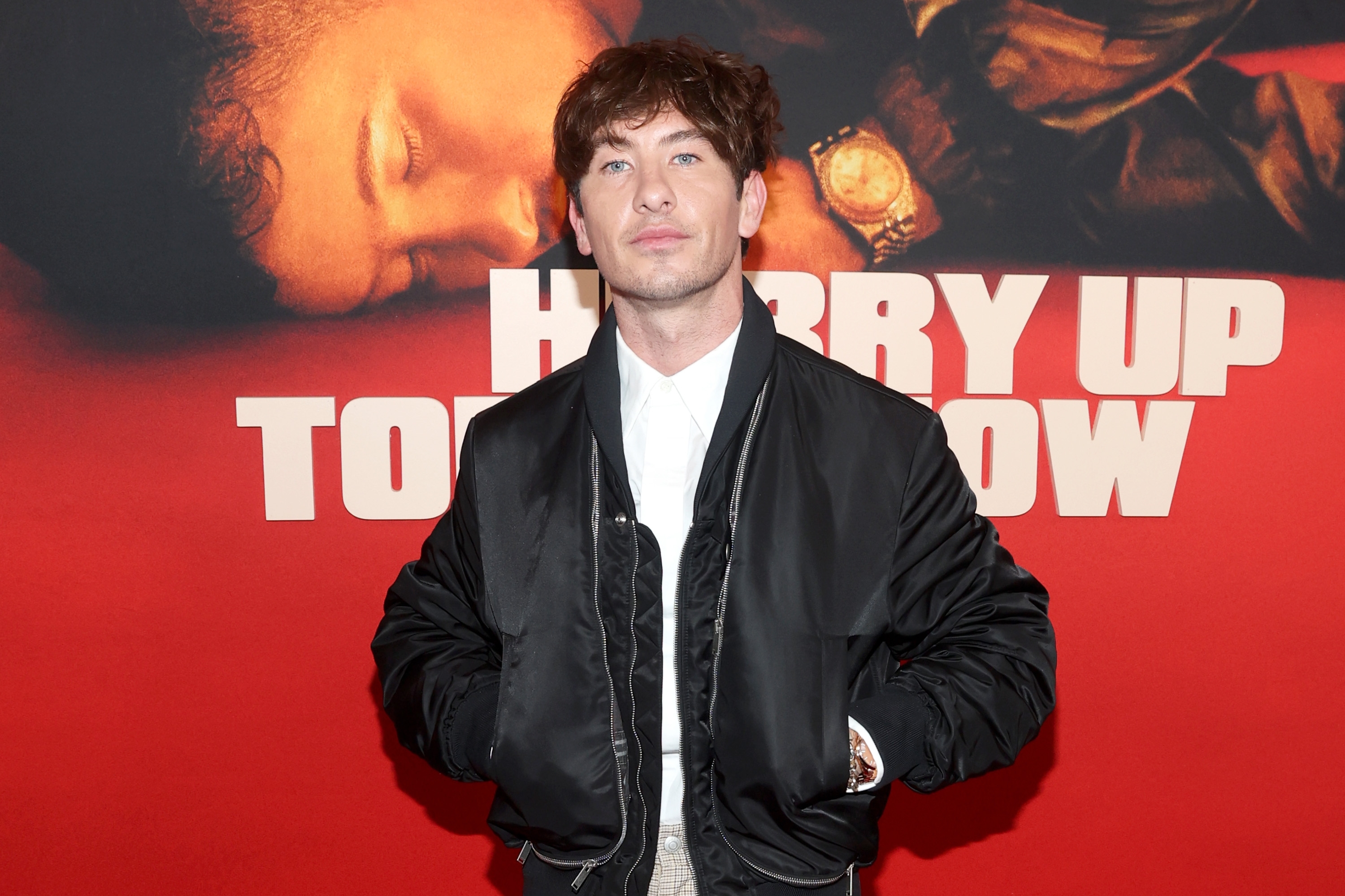 Barry Keoghan in a casual bomber jacket stands in front of a "Hurry Up Tomorrow" poster at an event