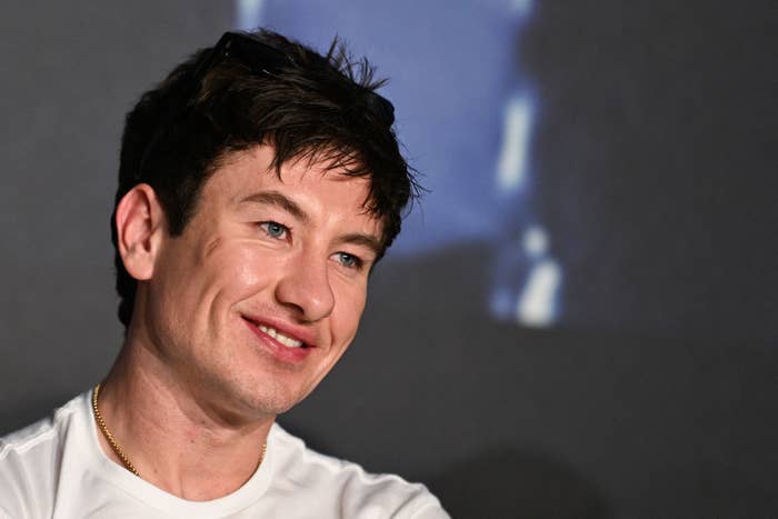 Barry Keoghan with short, dark hair and a white shirt is looking sideways, appearing at an event or interview
