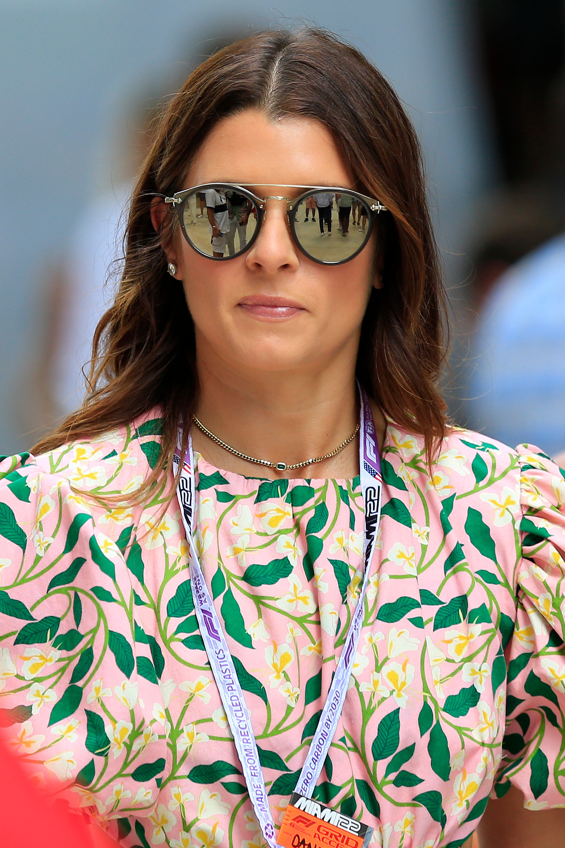 Danica Patrick wearing reflective sunglasses and a floral-patterned outfit with a lanyard around their neck