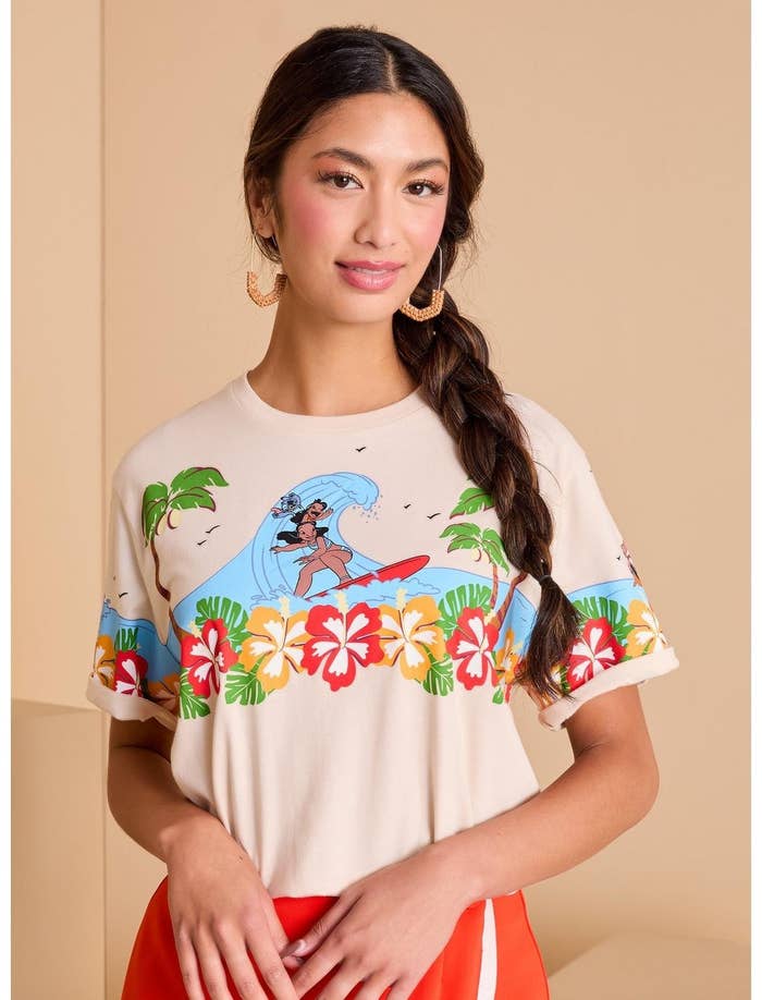 Person in floral-patterned surf-themed T-shirt stands in a neutral setting, showcasing casual summer fashion