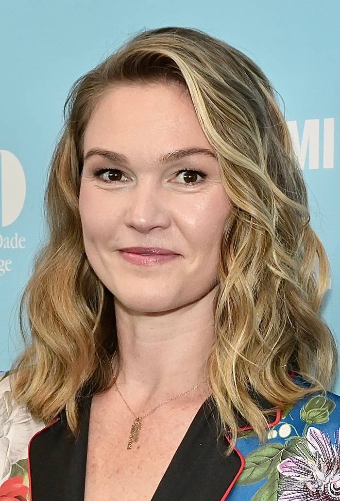 Person smiling at an event, wearing a floral-patterned jacket with wavy shoulder-length hair