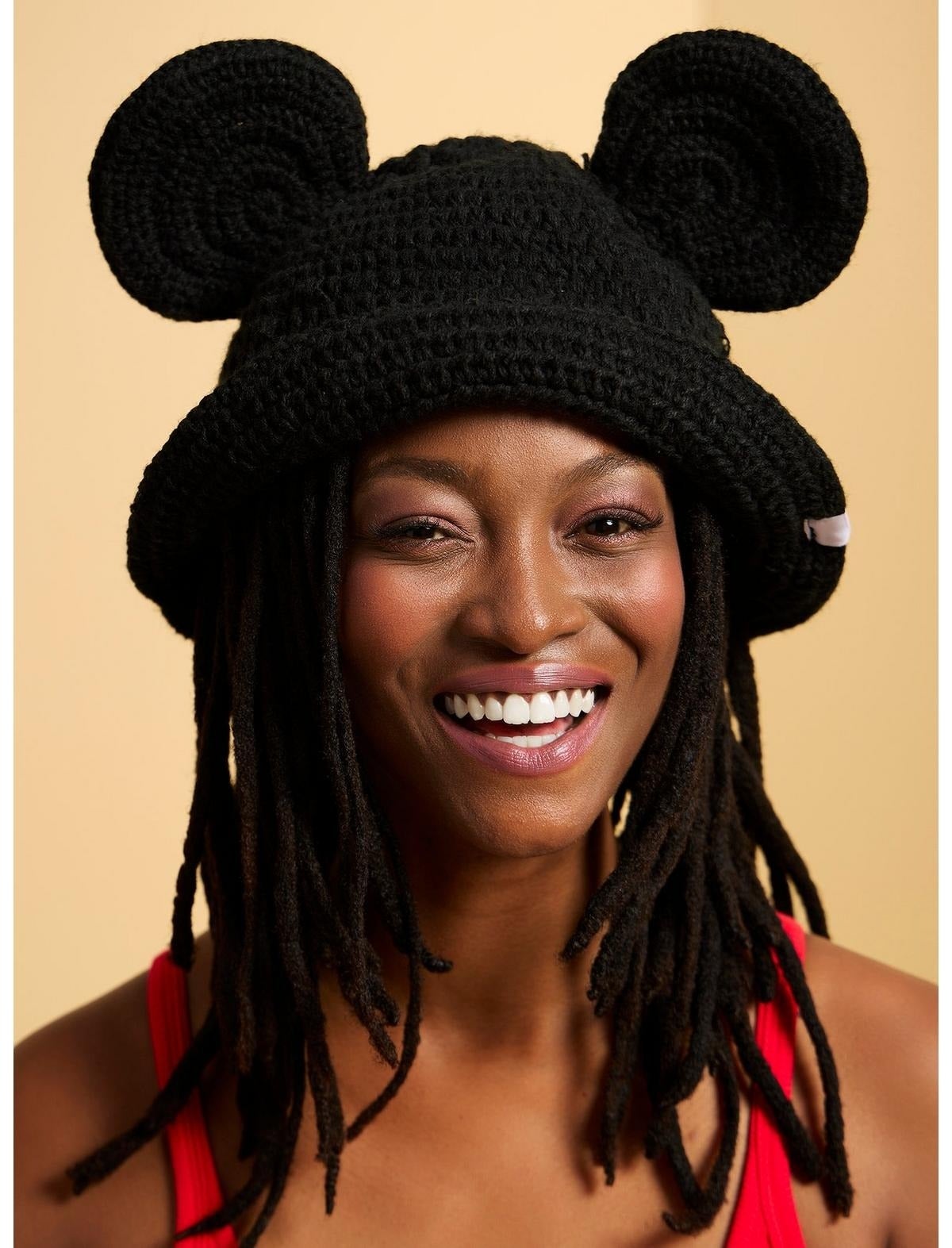 Person smiling, wearing a crocheted hat with large round ears and a sleeveless top. Fashionable and playful accessory ideal for unique styles