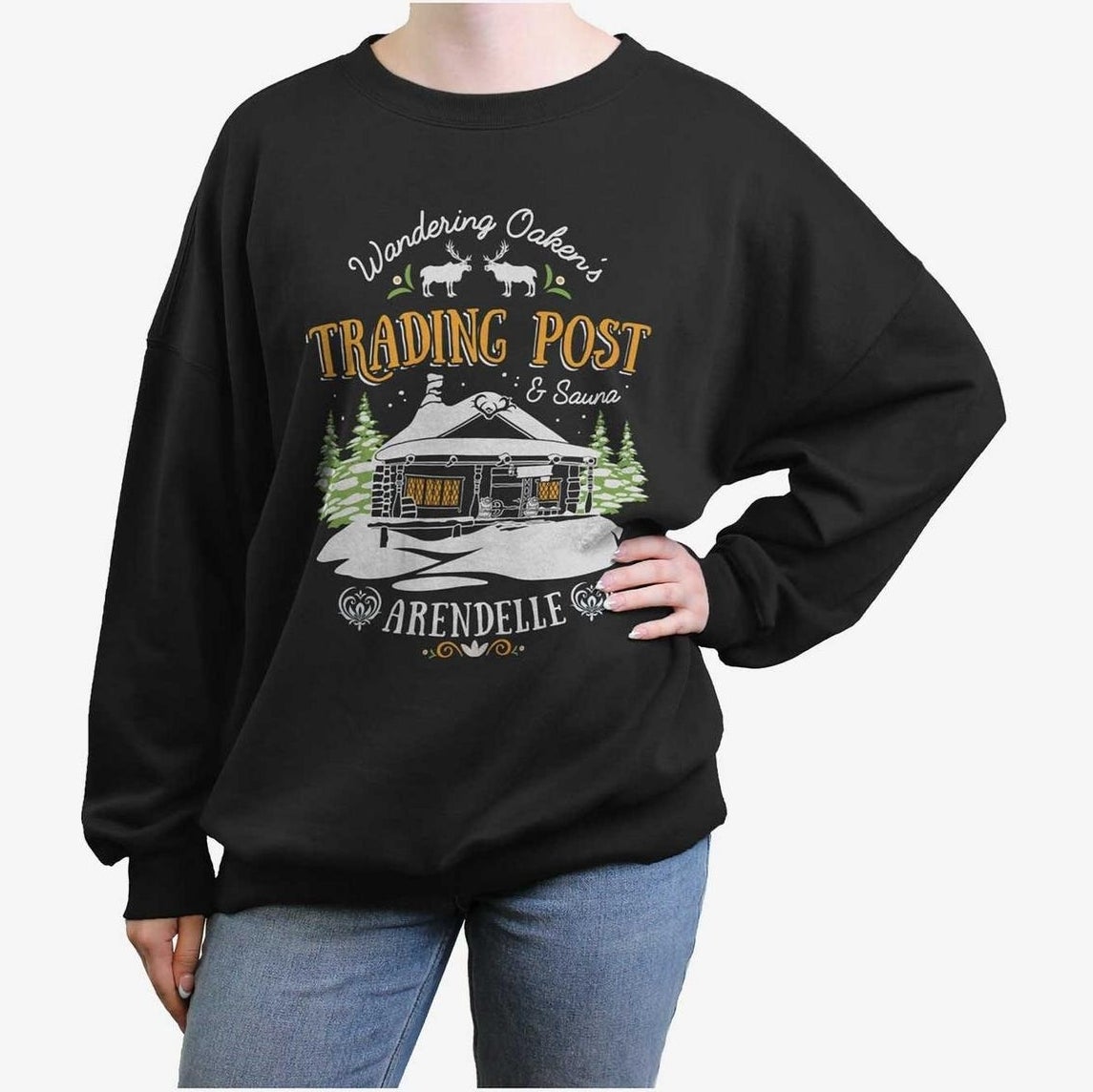 Person wearing a sweatshirt with a graphic of a trading post and the words "Wandering Oaken's Trading Post &amp;amp; Sauna, Arendelle," paired with jeans