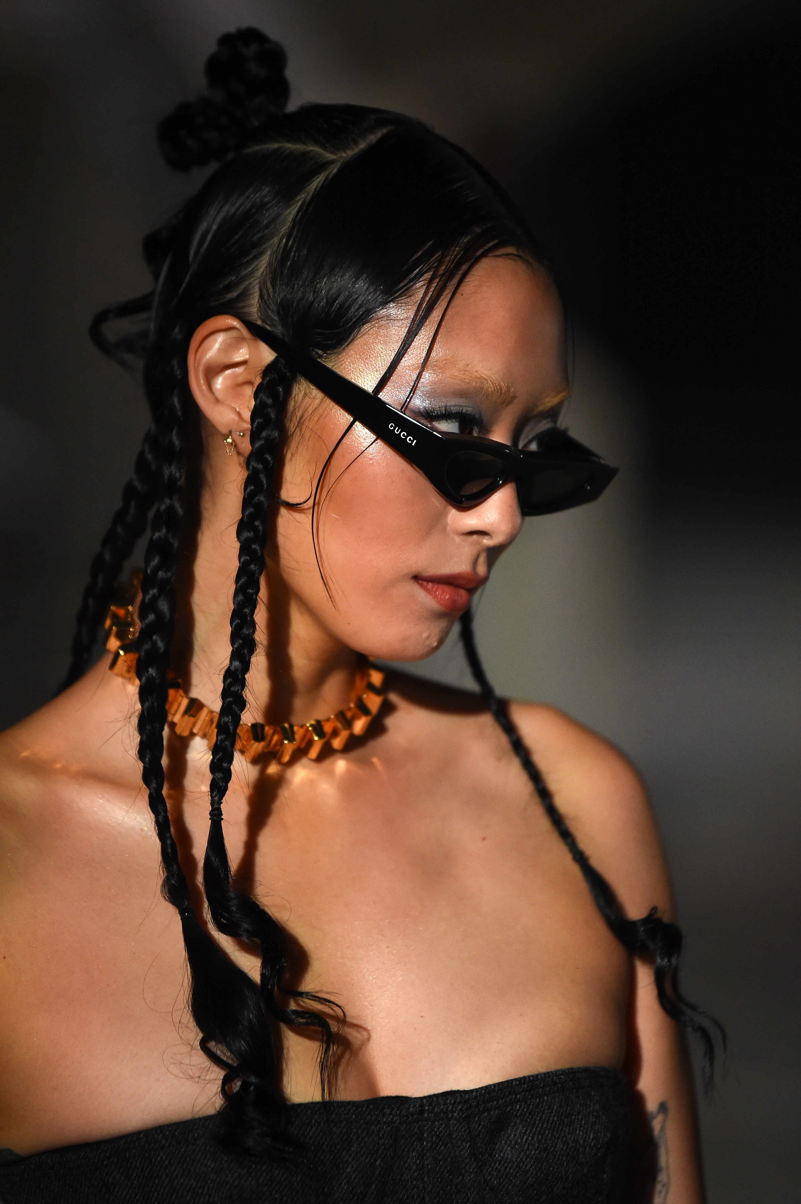 Person in stylish sunglasses with braided hair and a strapless top at a fashion event