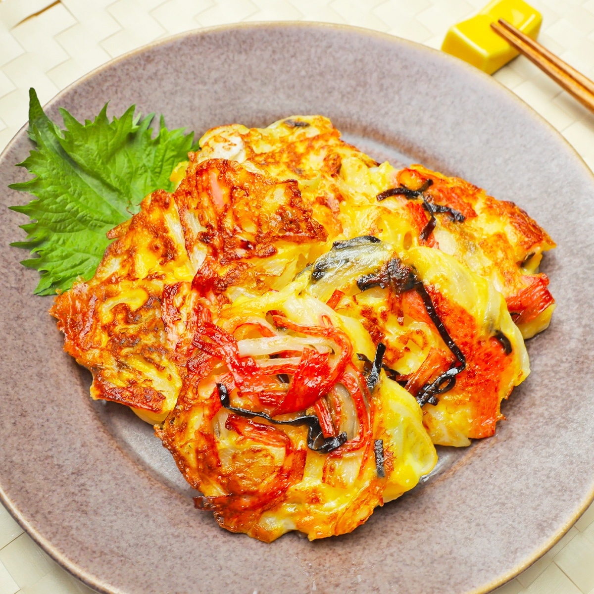 玉ねぎ料理が皿に盛られている。隣には箸と緑の葉が添えられている。