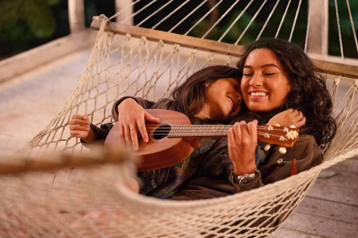 Two people are smiling and relaxing in a hammock. One is holding a ukulele