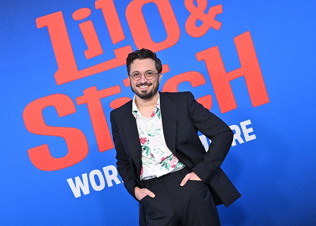 Person in a floral shirt and dark suit posing in front of a "Lilo & Stitch" premiere banner