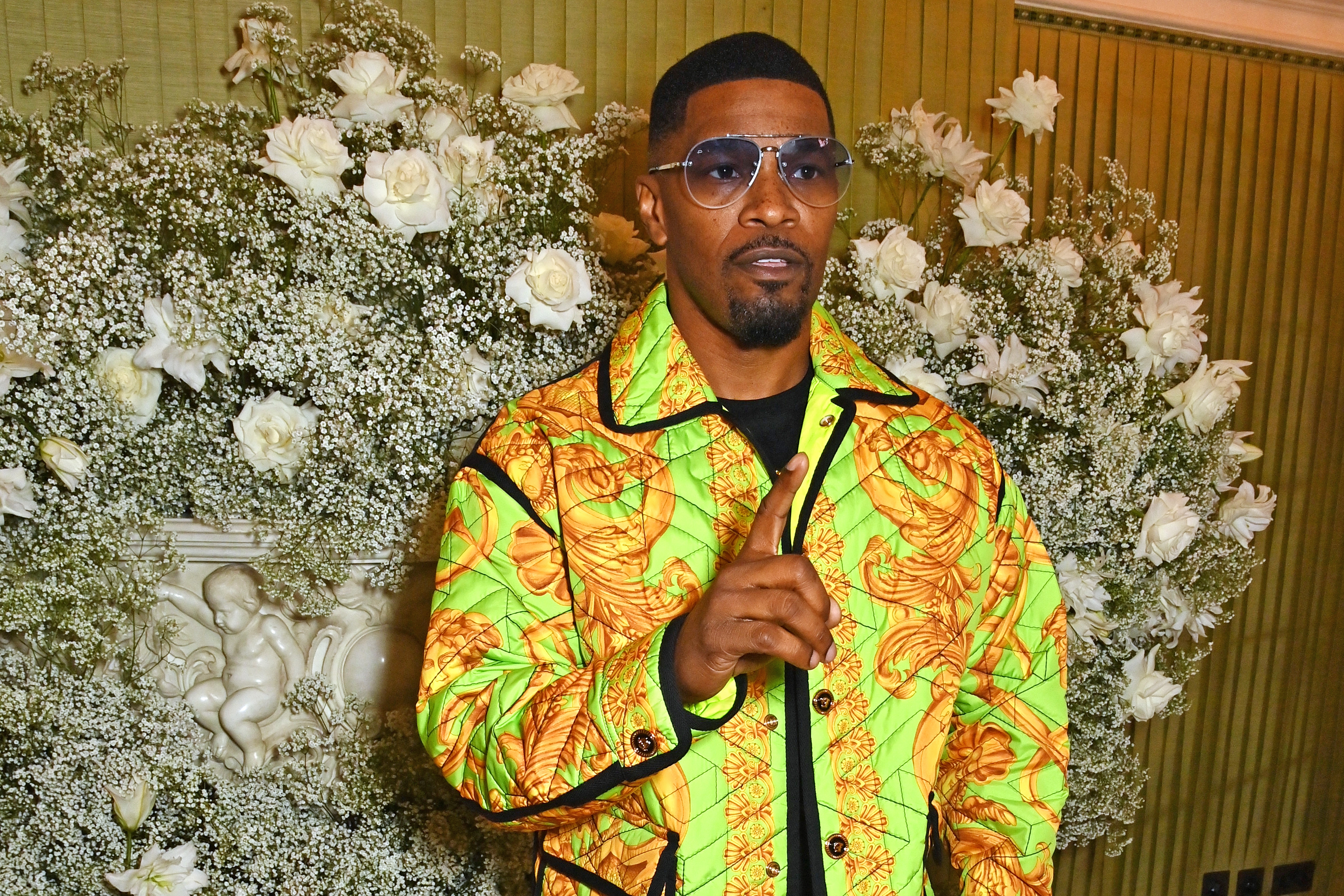 Jamie Foxx in a patterned suit gestures in front of floral background