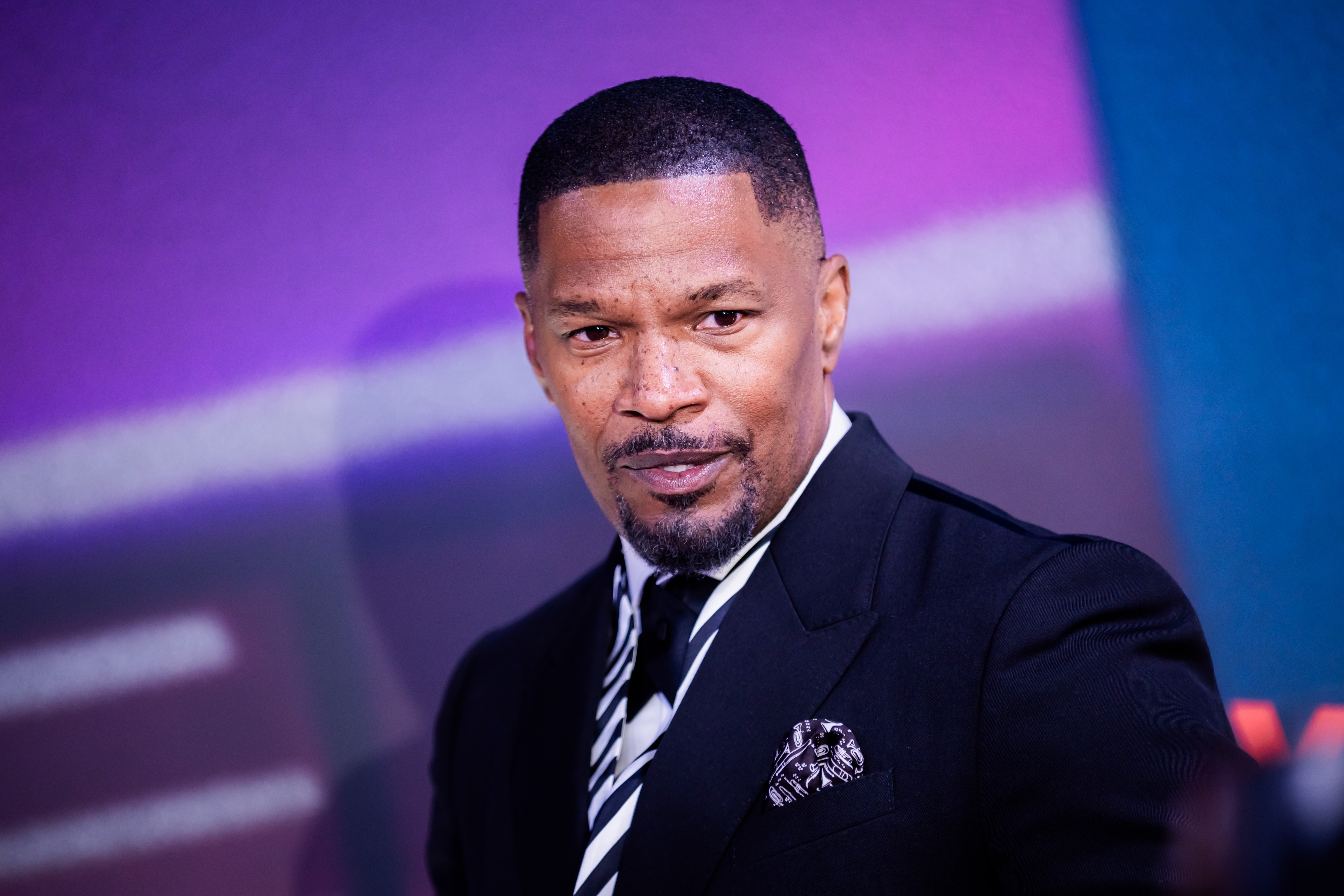 Jamie Foxx in a sharp suit with a striped tie, posing with a confident expression at an event