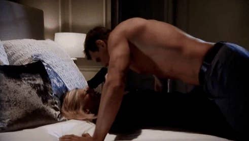 A shirtless man leans over a woman on a bed in an intimate setting, creating a dramatic and tense atmosphere