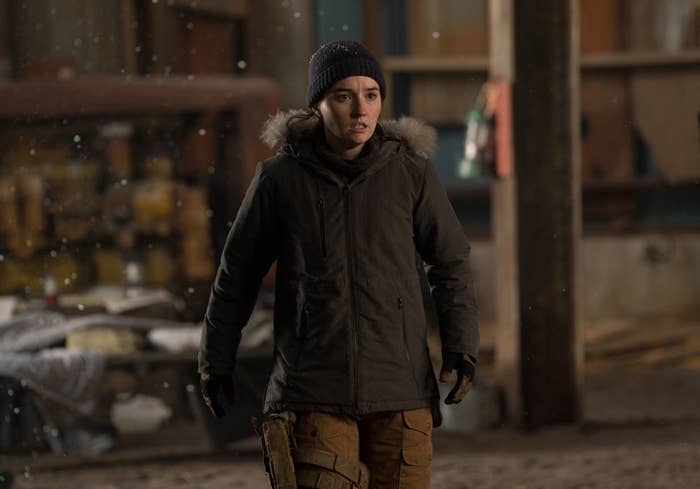 Persona con abrigo de invierno, gorro y guantes, en un ambiente industrial. Parece estar alerta o en movimiento