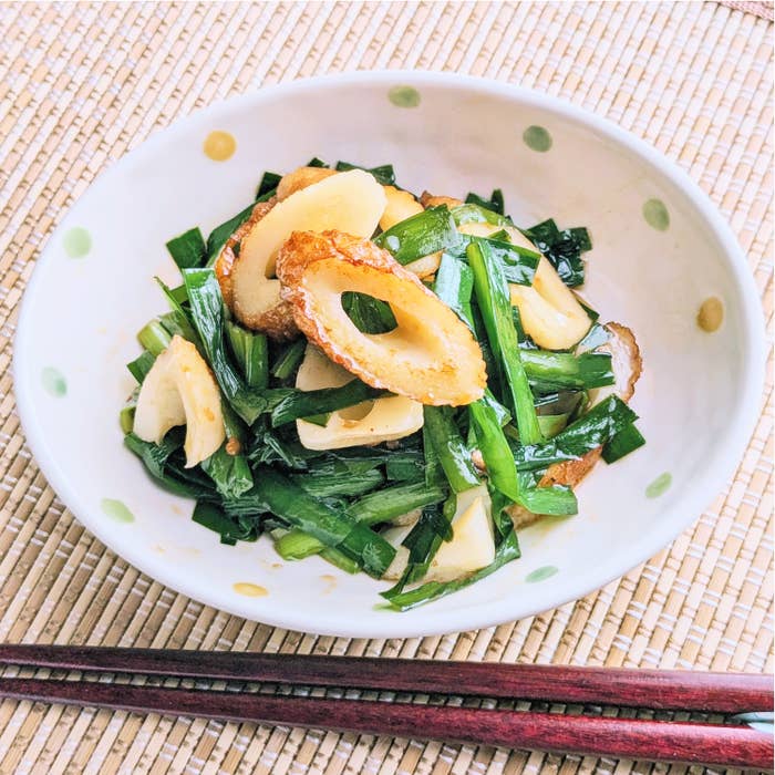 白い皿に盛られたニラとちくわの炒め物が置かれている。箸が横に置かれている。