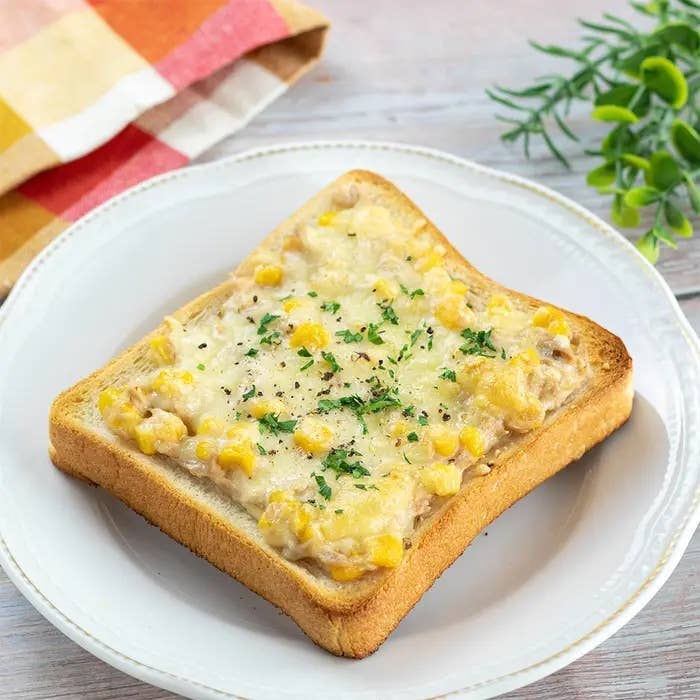 皿に盛られたトースト。チーズとコーンがトッピングされ、パセリが散らされています。横に布巾と植物が見える。