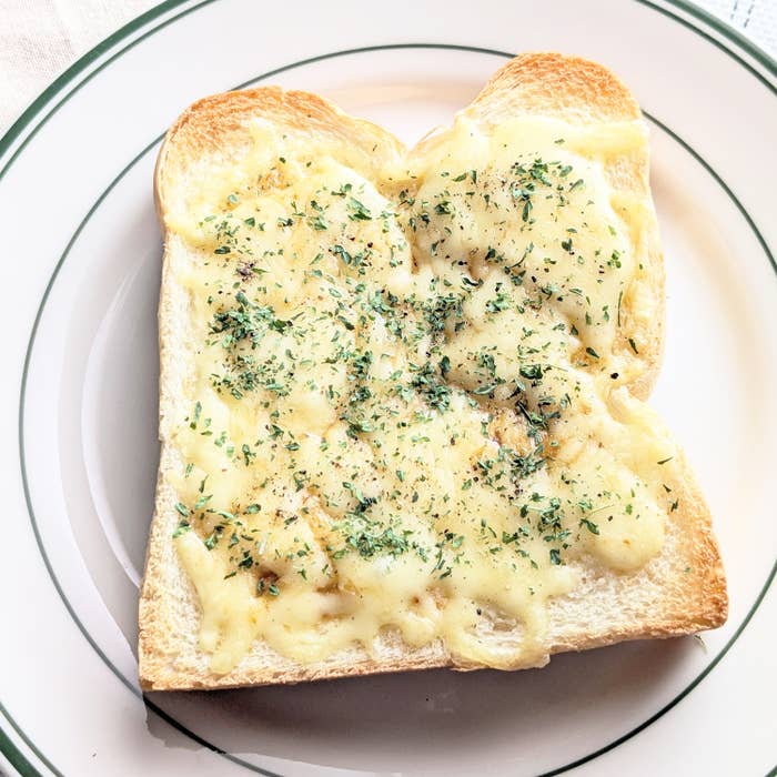パンの上にとろけたチーズとハーブがのったトーストが一枚、皿に置かれている。