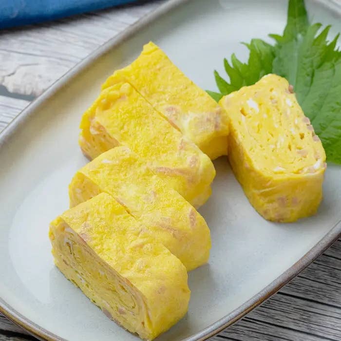 卵焼きが皿に盛られている様子。卵の層が重なっているのが見える。隣にシソの葉が添えられている。