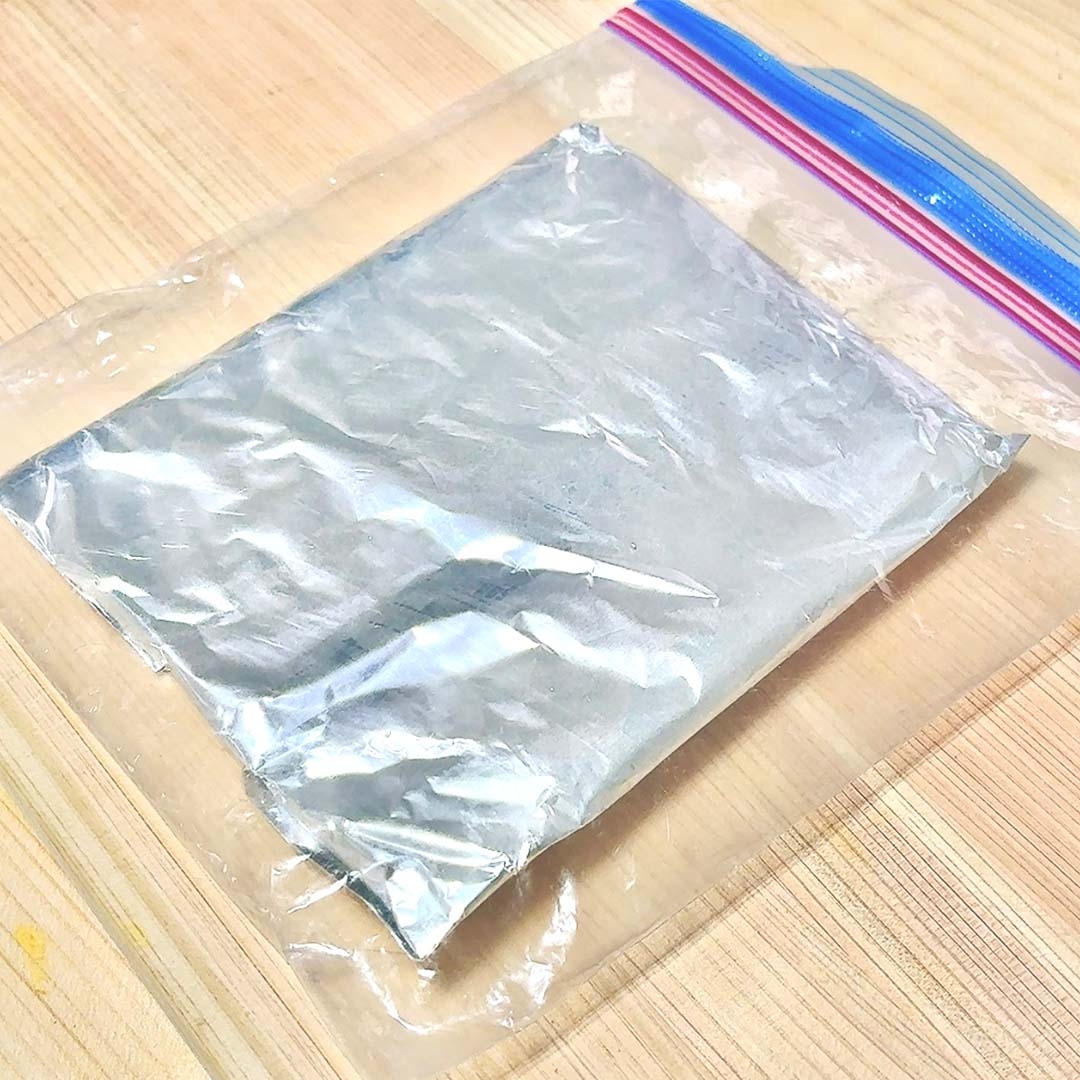 ジッパーバッグに入ったアルミホイルに包まれた物体が木製の表面に置かれている。