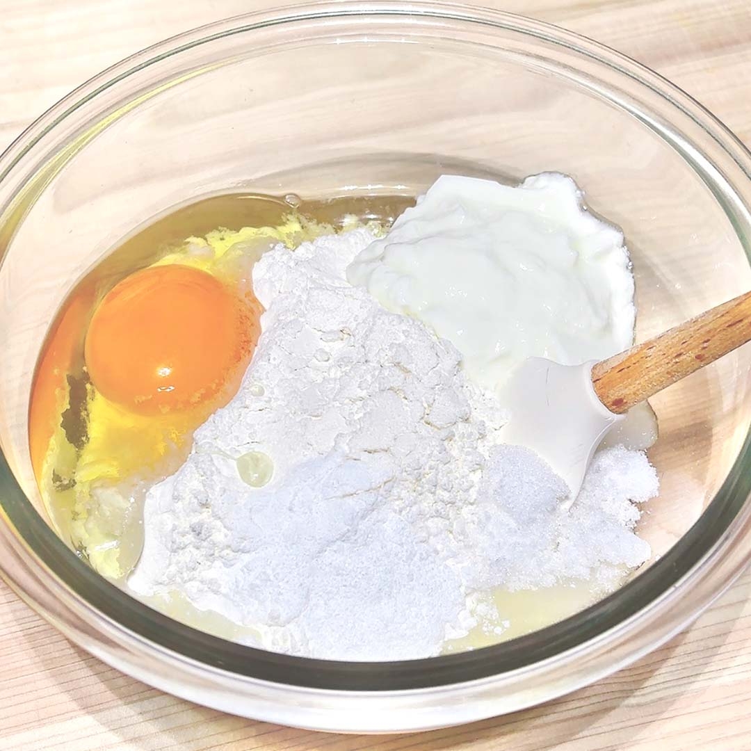 ボウルに卵、小麦粉、ヨーグルトが入っており、スパチュラで混ぜ始める準備がされている。