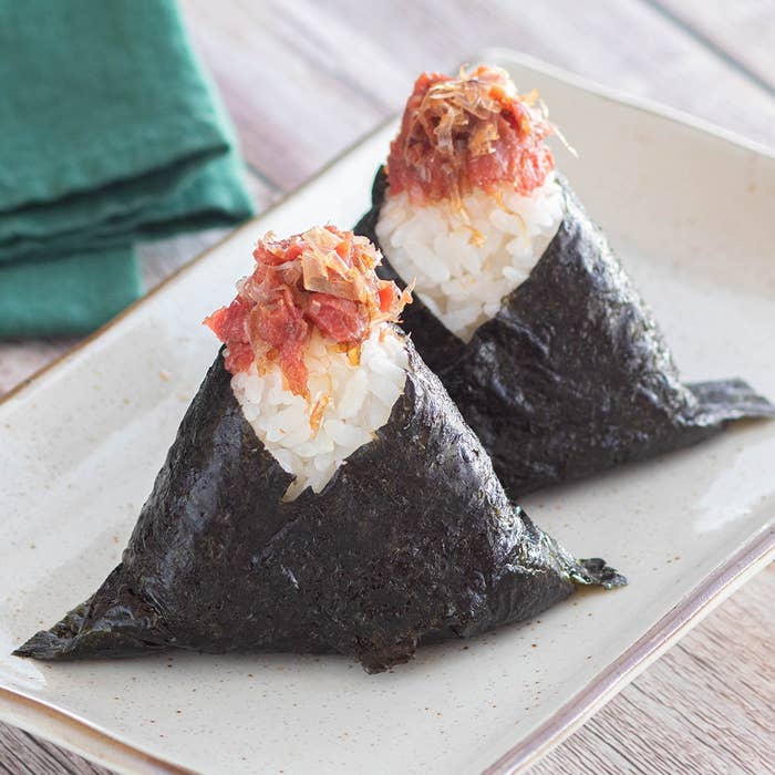 海苔で包まれたおにぎり2つ、上に具が載せられ、皿に盛られている。