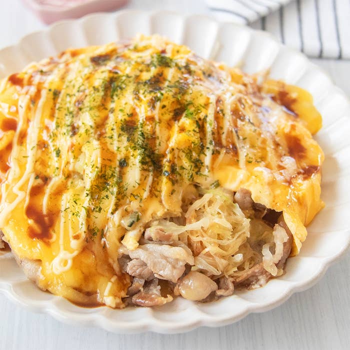 豚バラ肉、千切りキャベツ、卵で作られた包まないとんぺい焼きが皿に盛られている。ソースとマヨネーズ、青のりがかかっている。