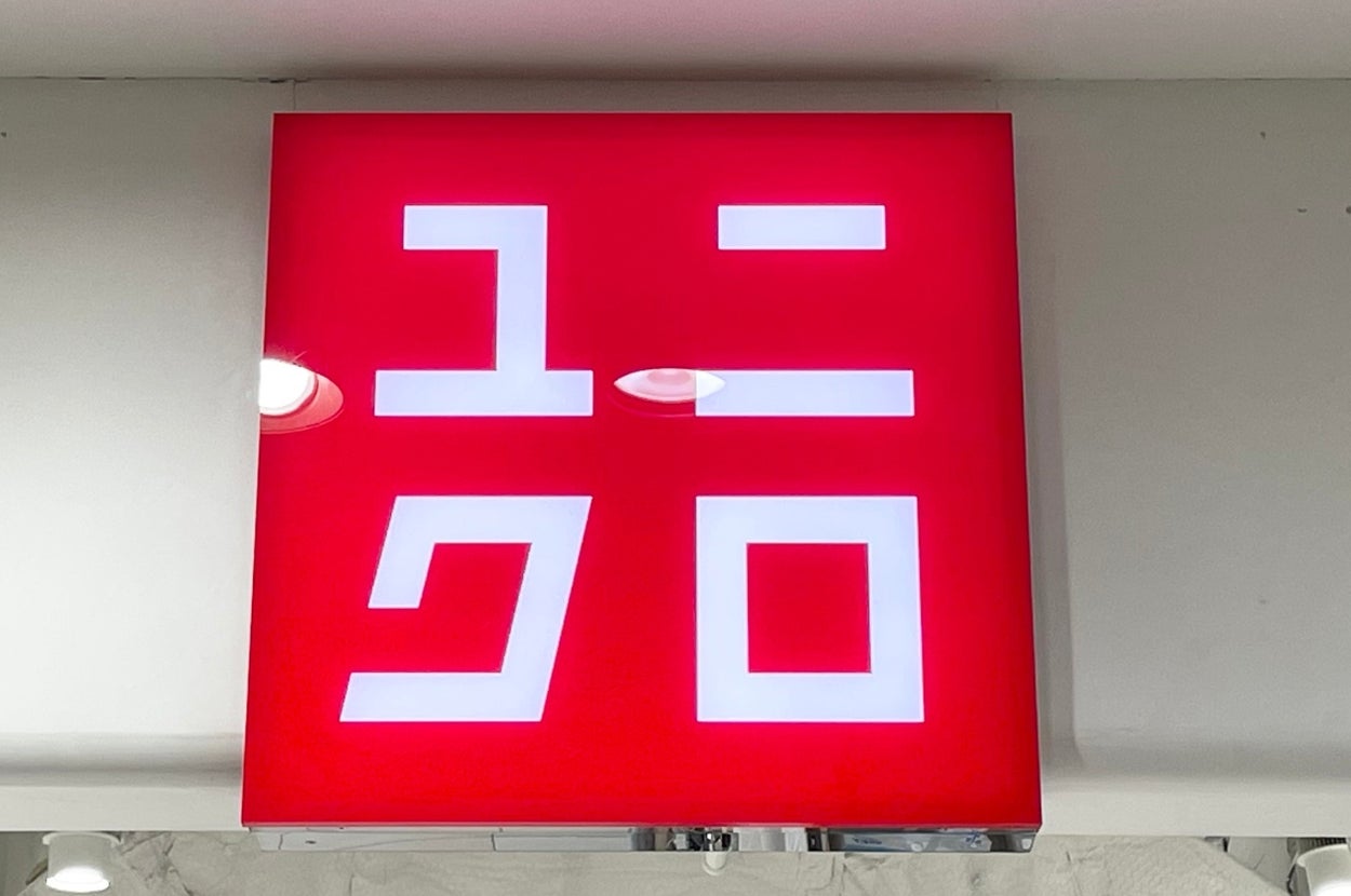 A square sign with Japanese characters resembling "Uniqlo" on it, mounted inside a building with visible ceiling fixtures