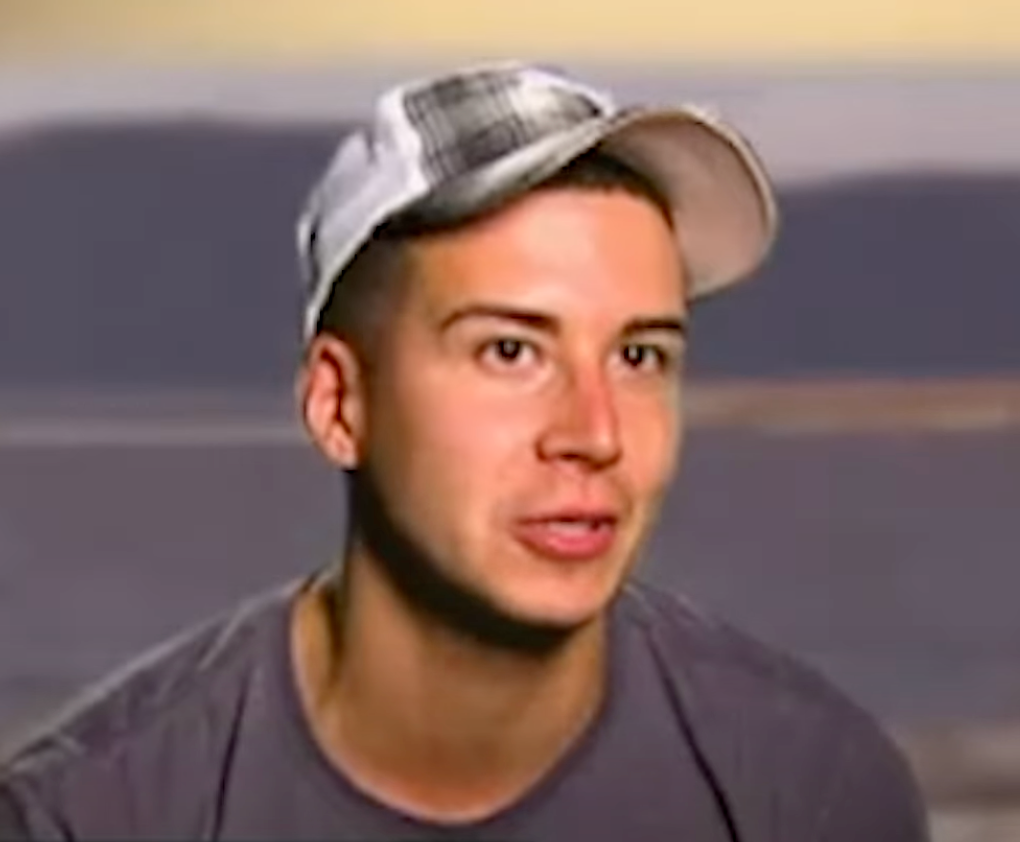 Person wearing a casual cap and t-shirt, speaking in an interview-style setting
