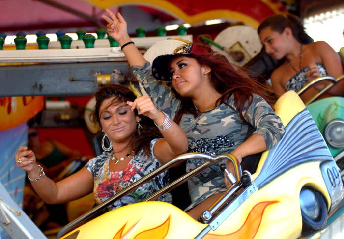 Two people on a fairground ride pose with peace signs, wearing casual and camo-patterned outfits, enjoying the experience