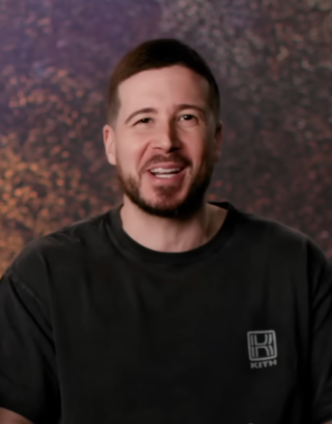 Man in a casual T-shirt smiles in front of a textured backdrop