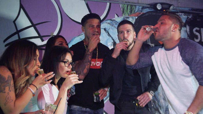 A group of people, including individuals in casual wear, are enjoying drinks together at an indoor event with a vibrant, graffiti-style backdrop
