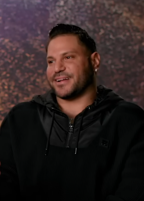 Person wearing a casual dark zip-up hoodie smiles against a textured backdrop