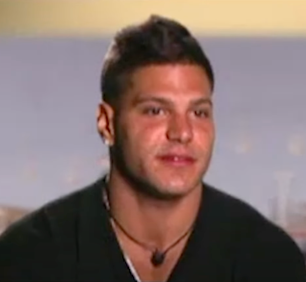 Person with short hair wearing a v-neck shirt and necklace, appearing in an interview setting