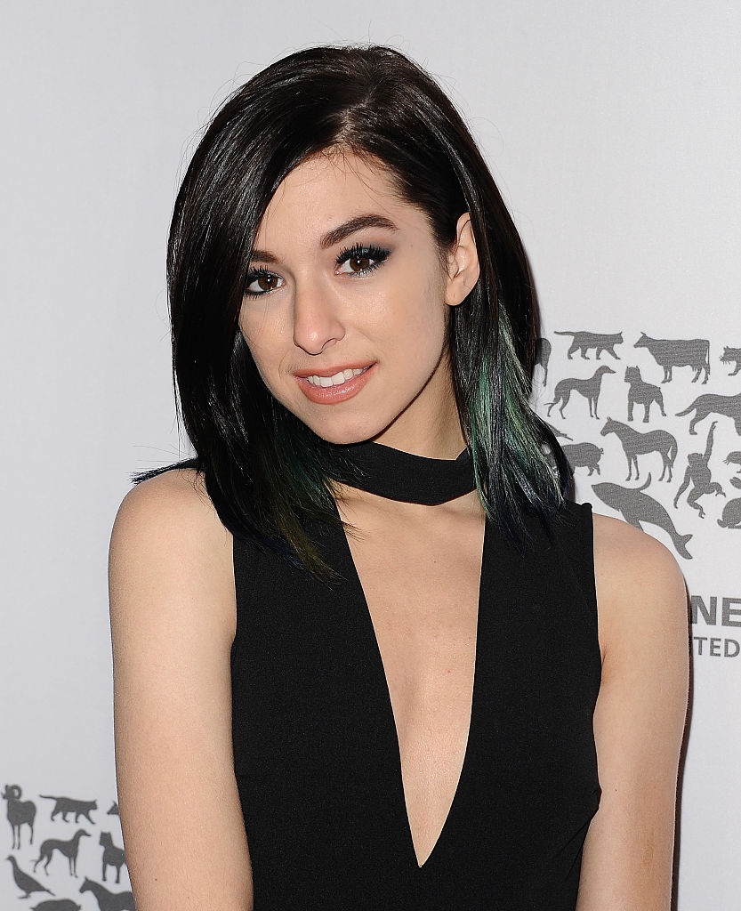 A person with shoulder-length hair and a smile wears a stylish black dress with a choker neckline, posing for a photo indoors with animal silhouettes