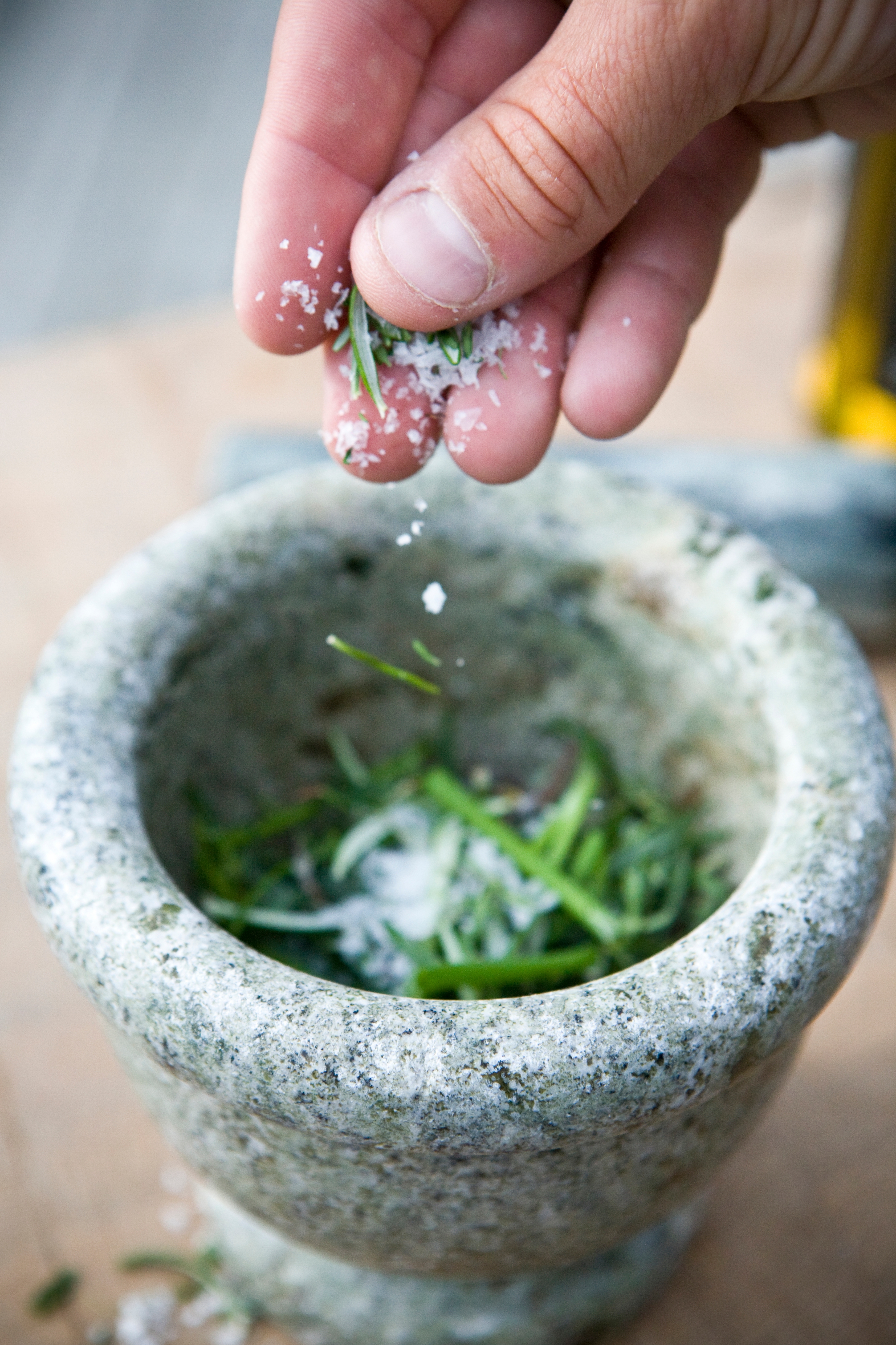 Hand sprinkling salt into stone mortar with herbs inside