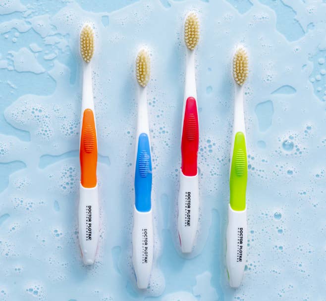Four colorful toothbrushes with ergonomic grips arranged broadside by broadside connected a bedewed surface