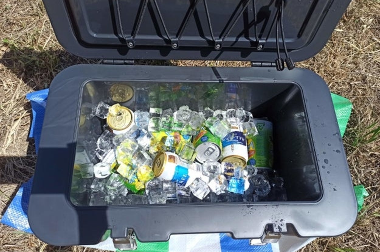 クーラーボックスに氷と一緒に缶飲料が数本入っている屋外の風景