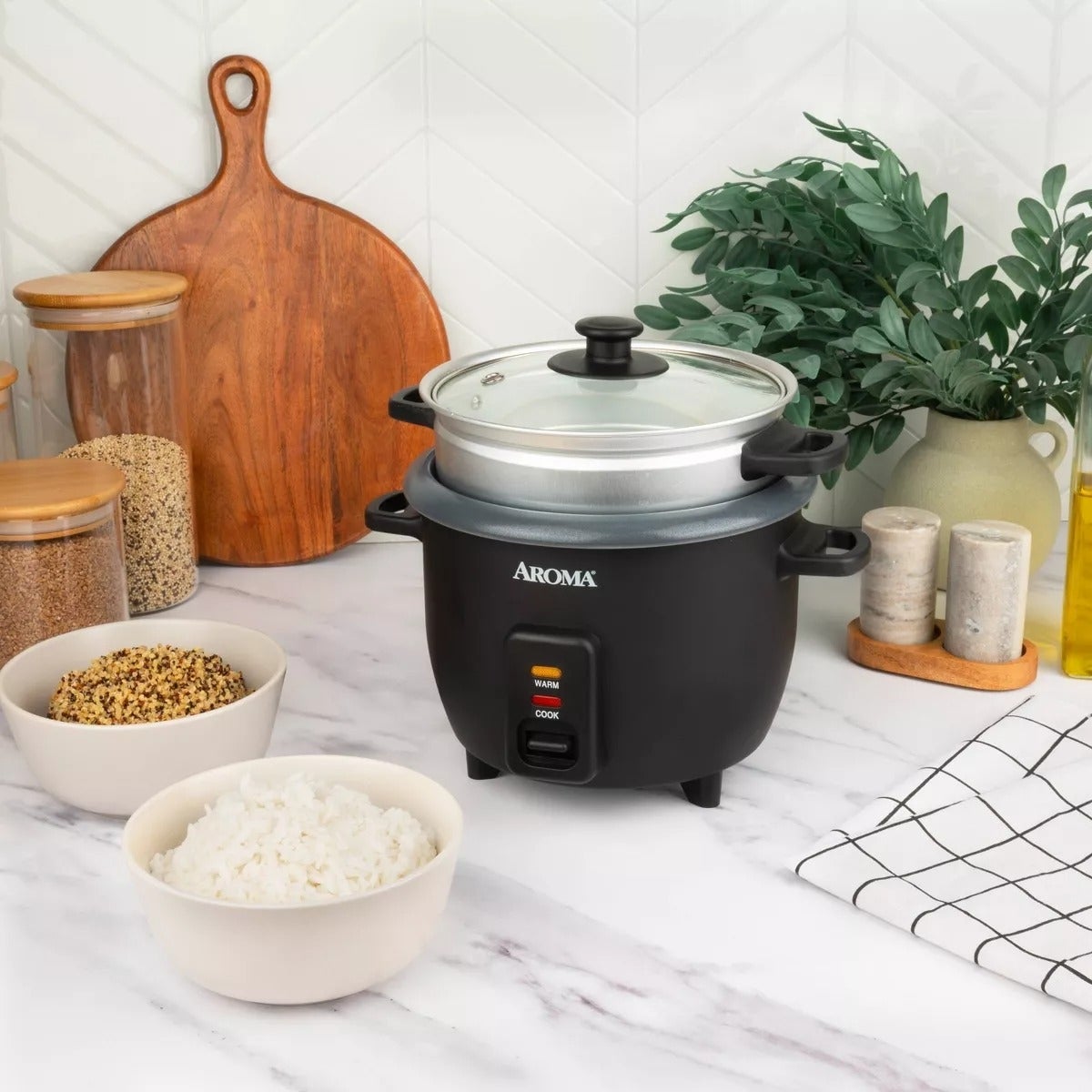 Adegan dapur meja dengan penanak nasi aroma hitam, mangkuk nasi dan biji -bijian, talenan, dan tanaman