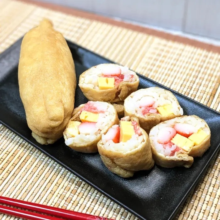 寿司ロールが黒いプレートに盛られている。具材にはエビと豆腐が見える。側には箸が置かれている。