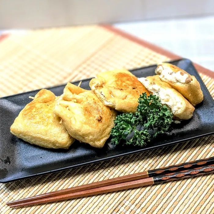 黒い皿に盛られた揚げ餃子が4つあり、緑の飾りが添えられている。箸が横に置かれている。