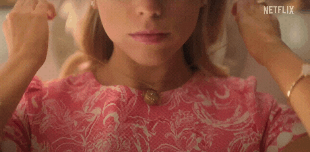 A person wearing a patterned dress adjusts their hair while looking in a mirror