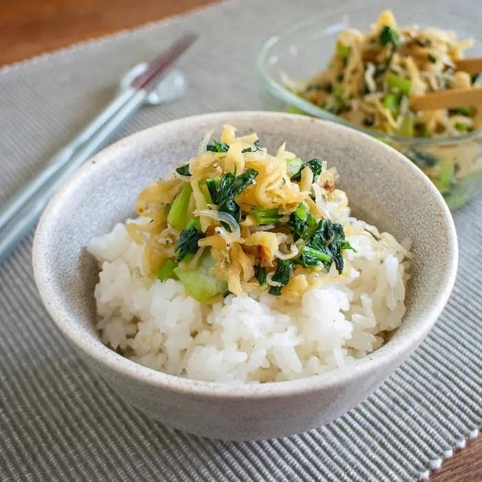 ご飯の上にネギと野菜のトッピングがのった丼がテーブルに置かれている。横には菜箸が置かれている。