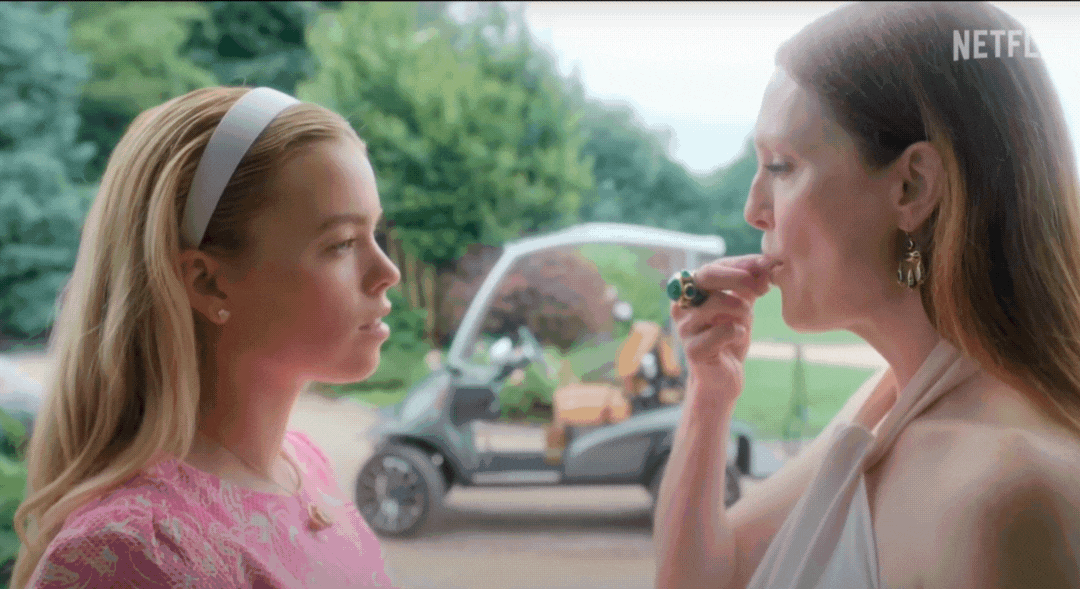 Two women outdoors: one in a pink patterned top with a headband, the other in a white one-shoulder top, gesturing with a hand near her face