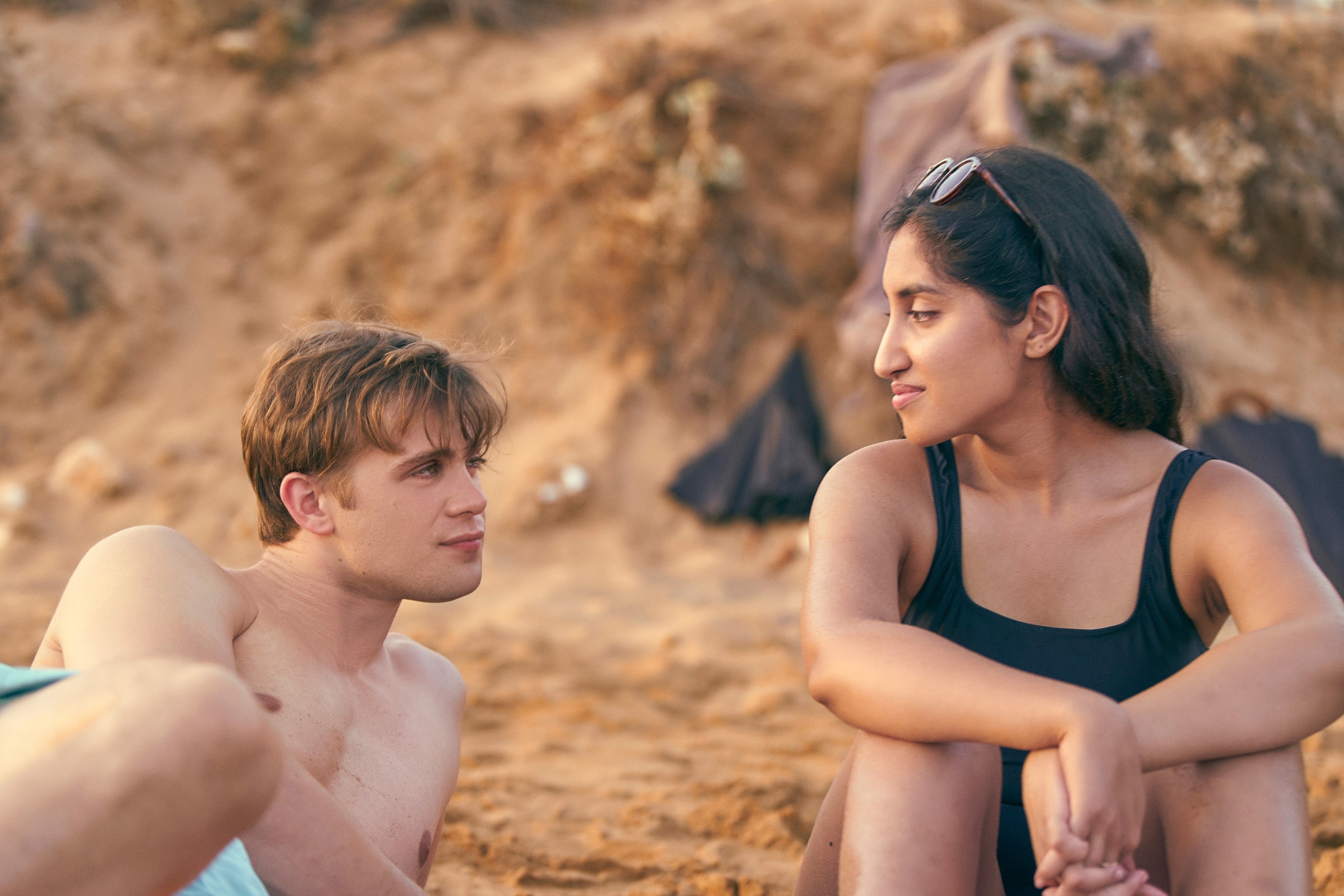 Leo Woodall and Ambika Mod sitting on a sandy beach in a scene from "One Day"