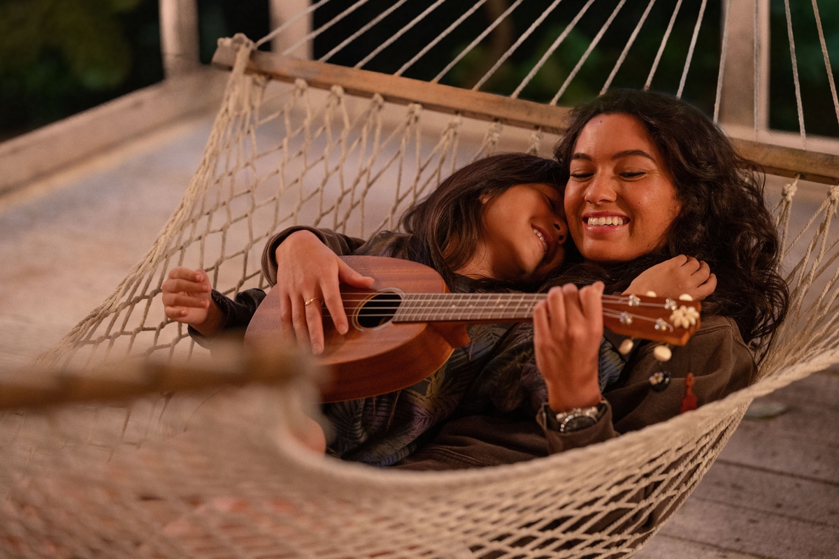 Lilo and Nani smiling while realxing in a hammock and playing music in a scene from the live-action Lilo and Stitch