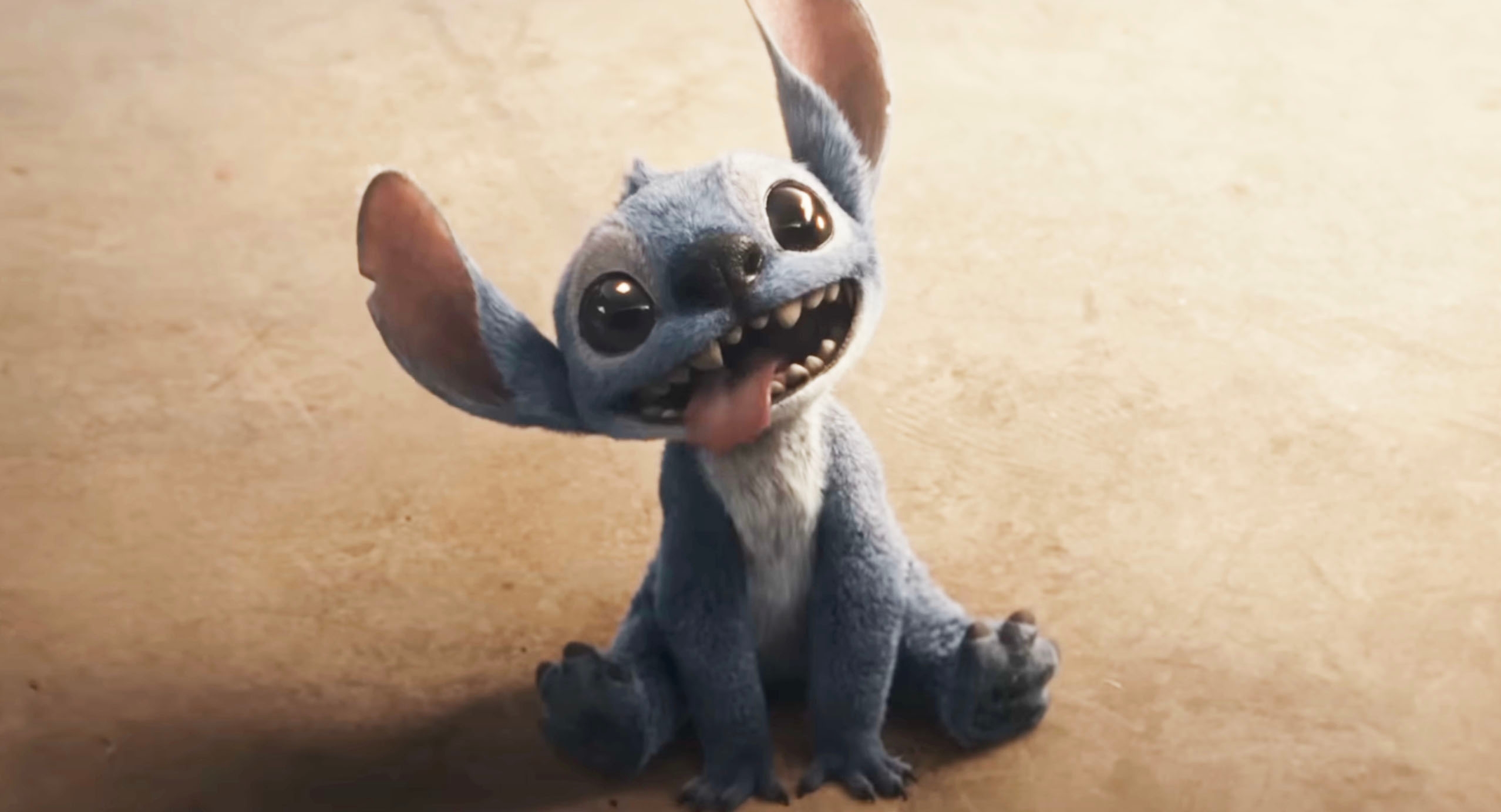 Stitch sits on the ground with a playful expression and tongue out