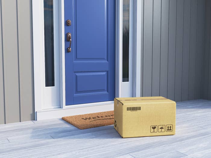 A cardboard box sits on a welcome mat in front of a blue door on a porch