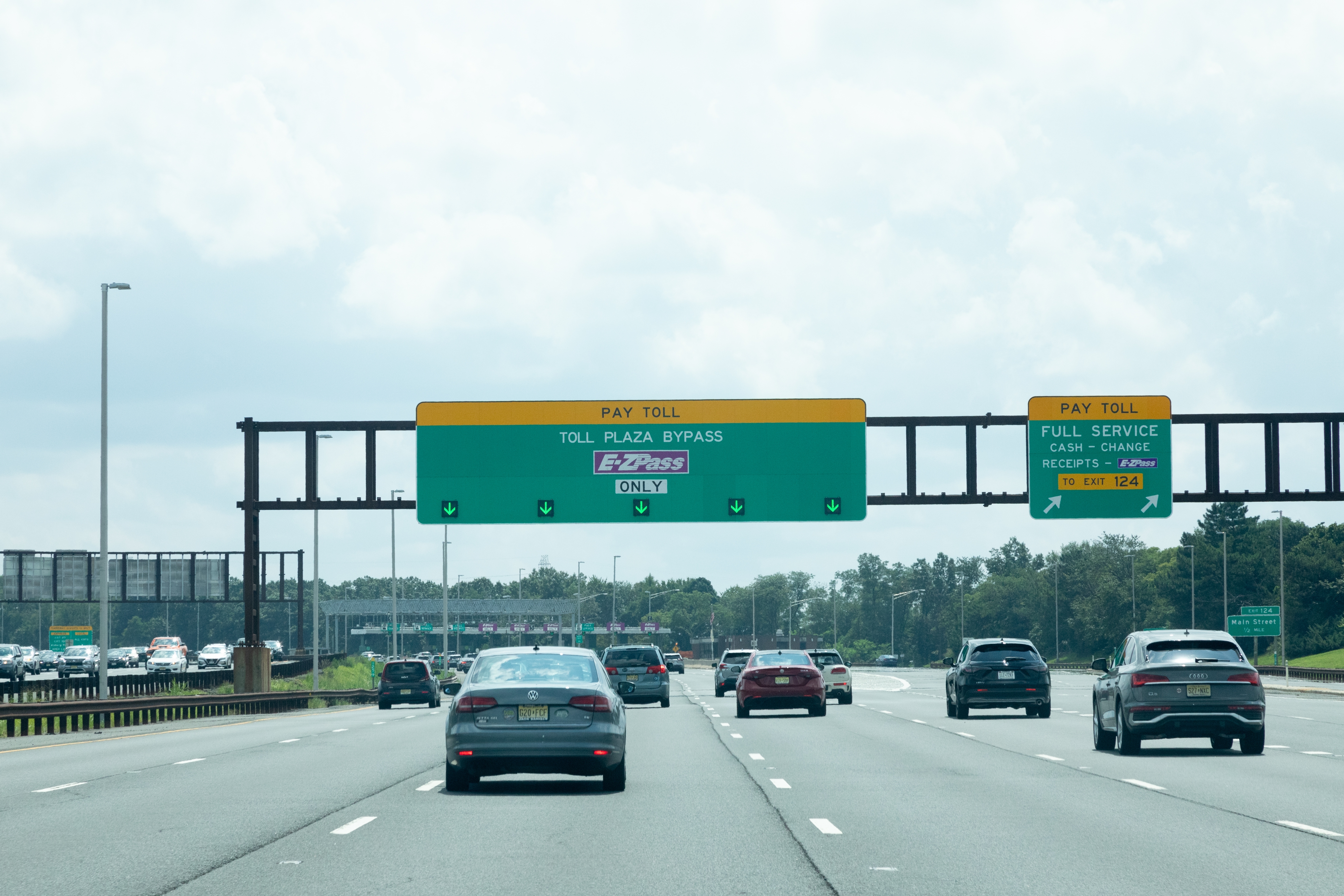 Highway scene with cars approaching a toll booth, overhead signs showing toll options and EZ Pass lanes
