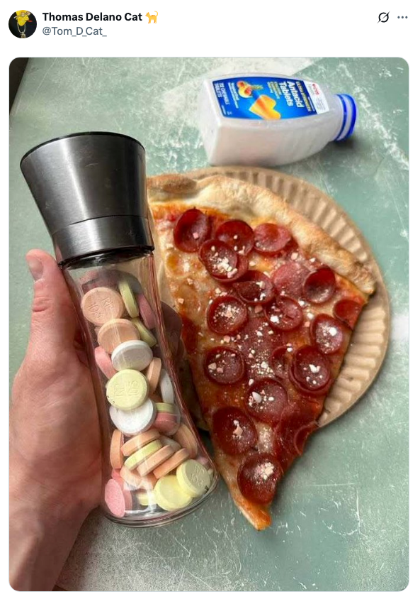 A hand holds a grinder filled with candy, positioned over a slice of pepperoni pizza on a paper plate. A small milk carton is in the background