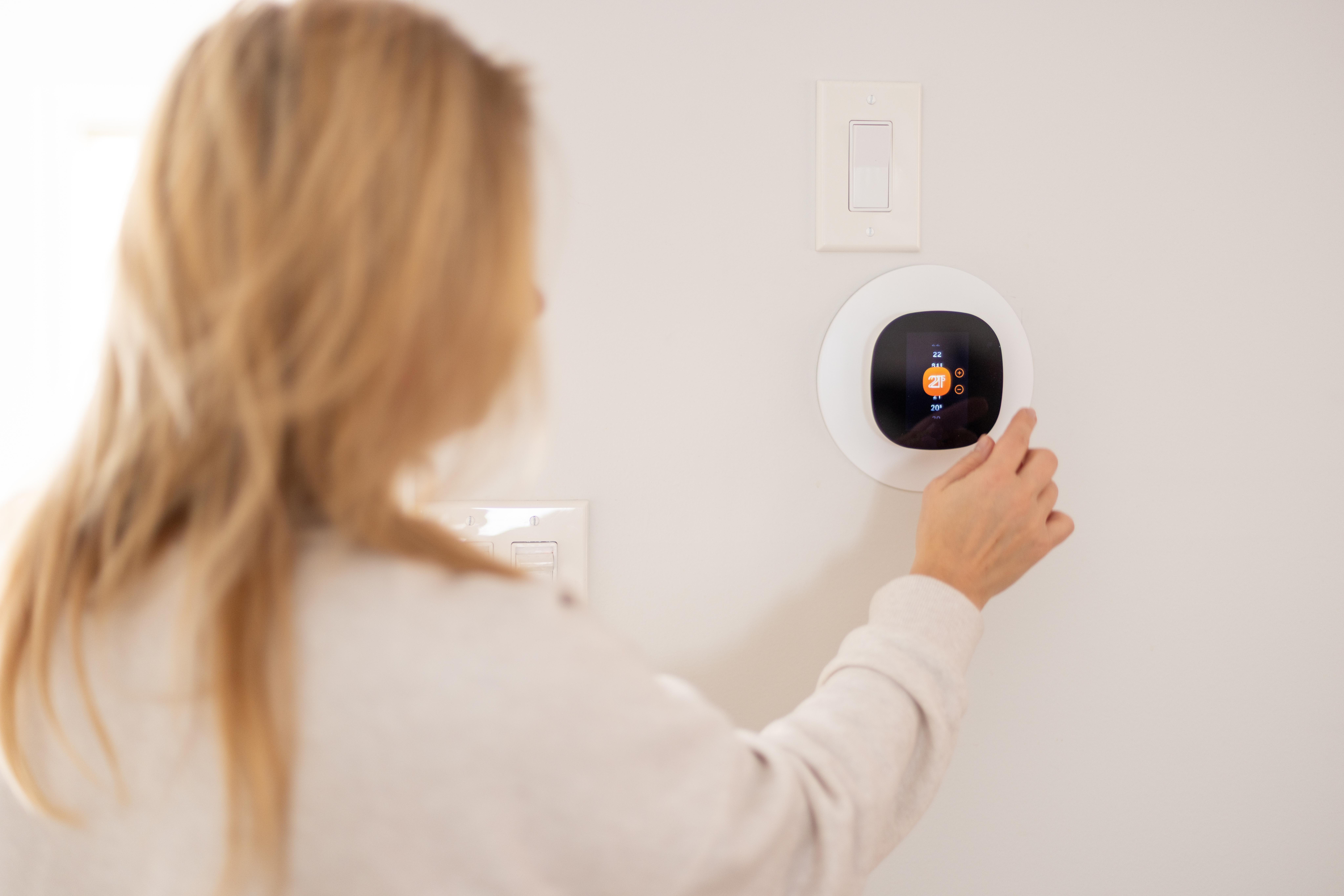Person adjusting a smart thermostat on a wall, focused on the display