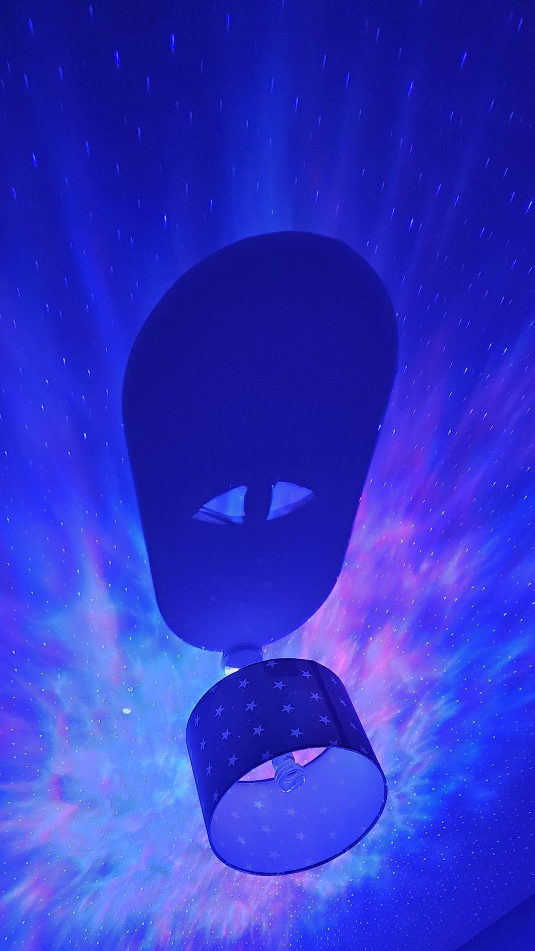 Ceiling lamp with star-patterned shade casting shadow amidst starry night sky projection