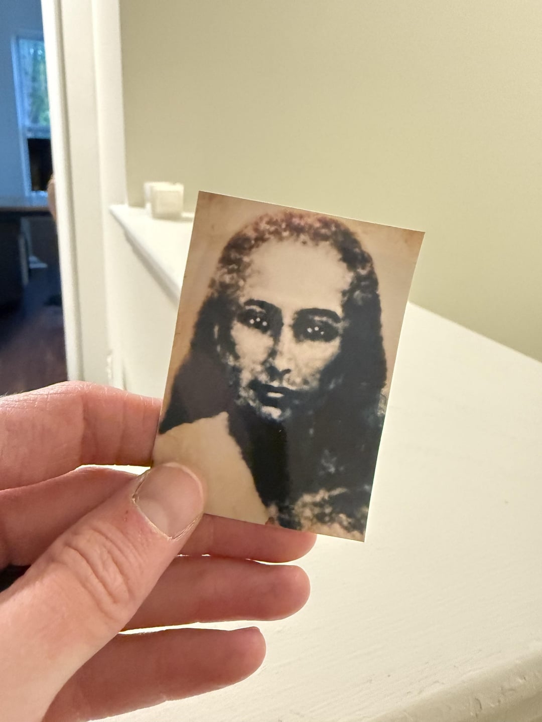 A hand holds an old, blurred photograph of a woman with long hair